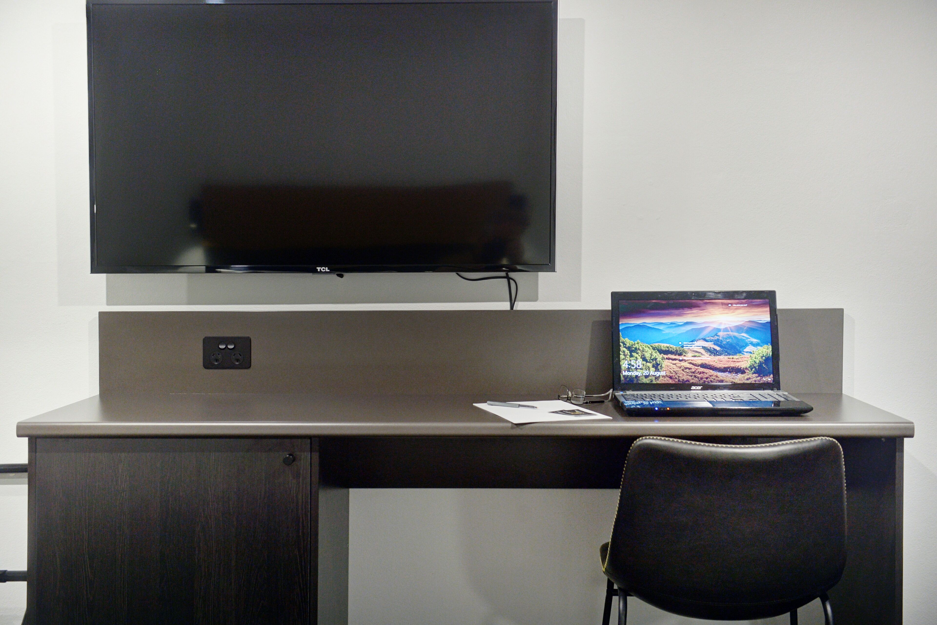 A desk with a laptop, a flat-screen TV, and a chair.