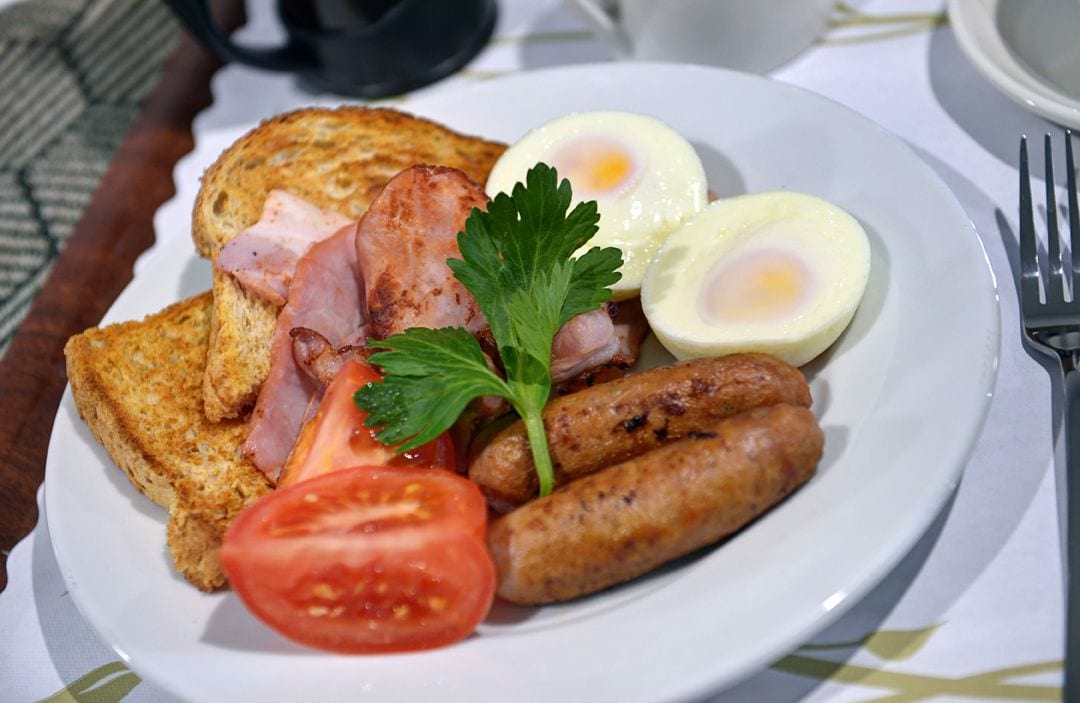 A plate of breakfast food including toast, eggs, sausages, and a tomato slice.