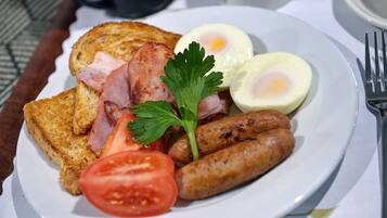 A plate of breakfast food including toast, eggs, sausages, and a tomato slice.