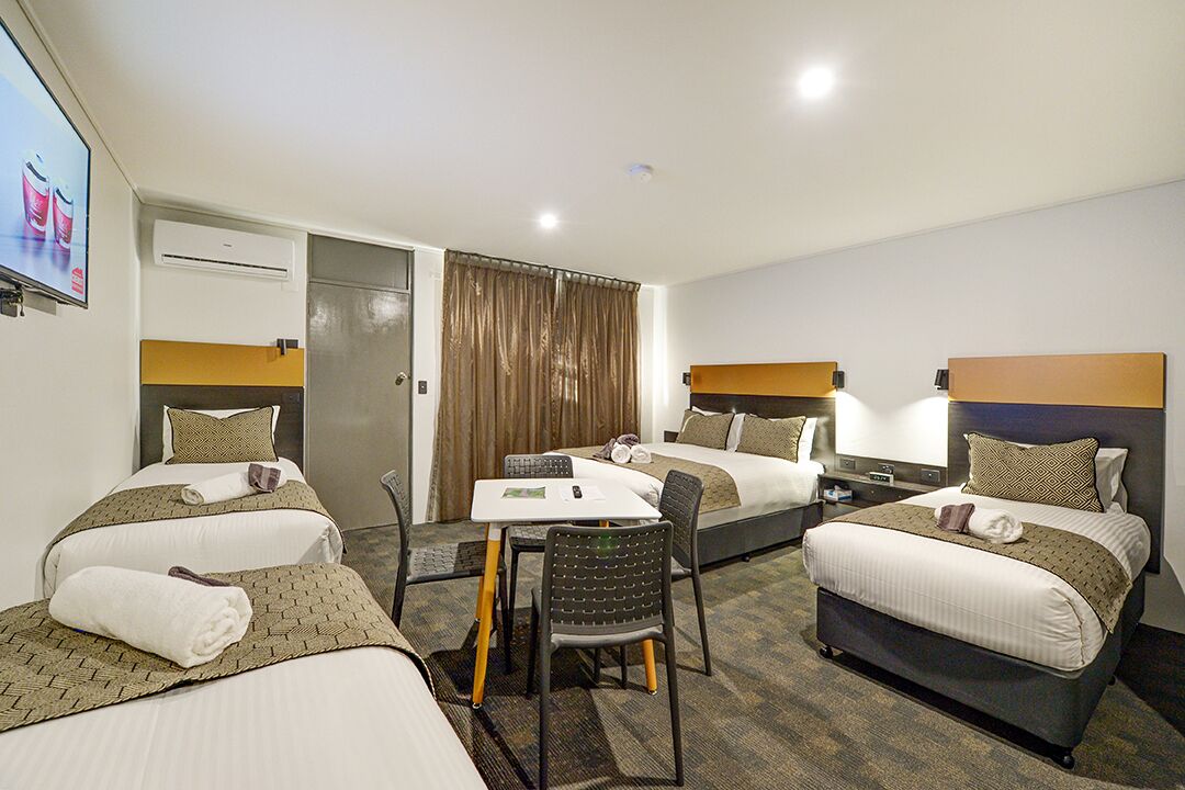 A hotel room with two beds, a small table, and a chair. There is a TV mounted on the wall and an air conditioning unit above the door.