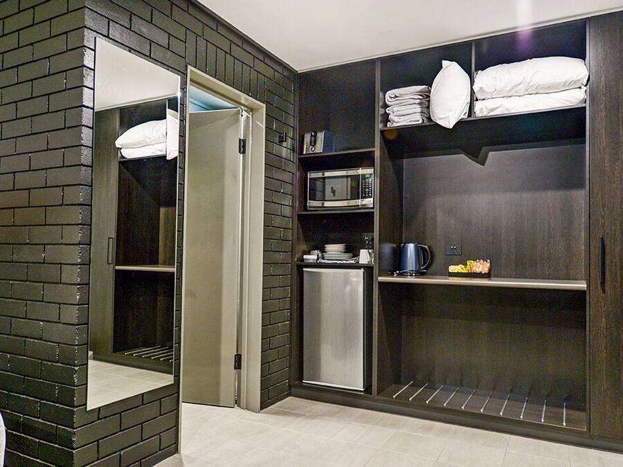 A modern hotel room with a dark wood wardrobe, a built-in microwave, and a small refrigerator.