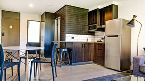 A modern kitchen with a central island, dark wooden cabinets, a stainless steel refrigerator, and a dining area with a round table and chairs.