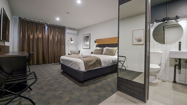 A hotel room with a bed, desk, chair, and a bathroom with a toilet and sink.