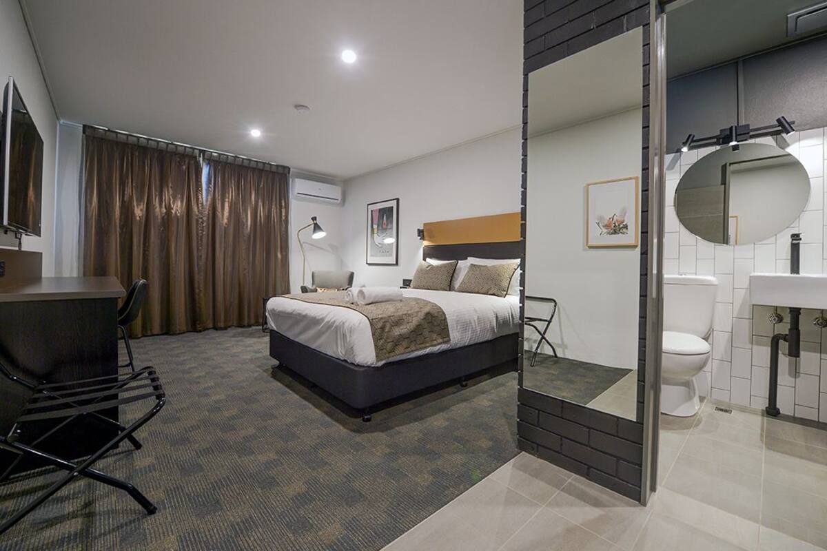 A hotel room with a bed, desk, chair, and a bathroom with a toilet and sink.