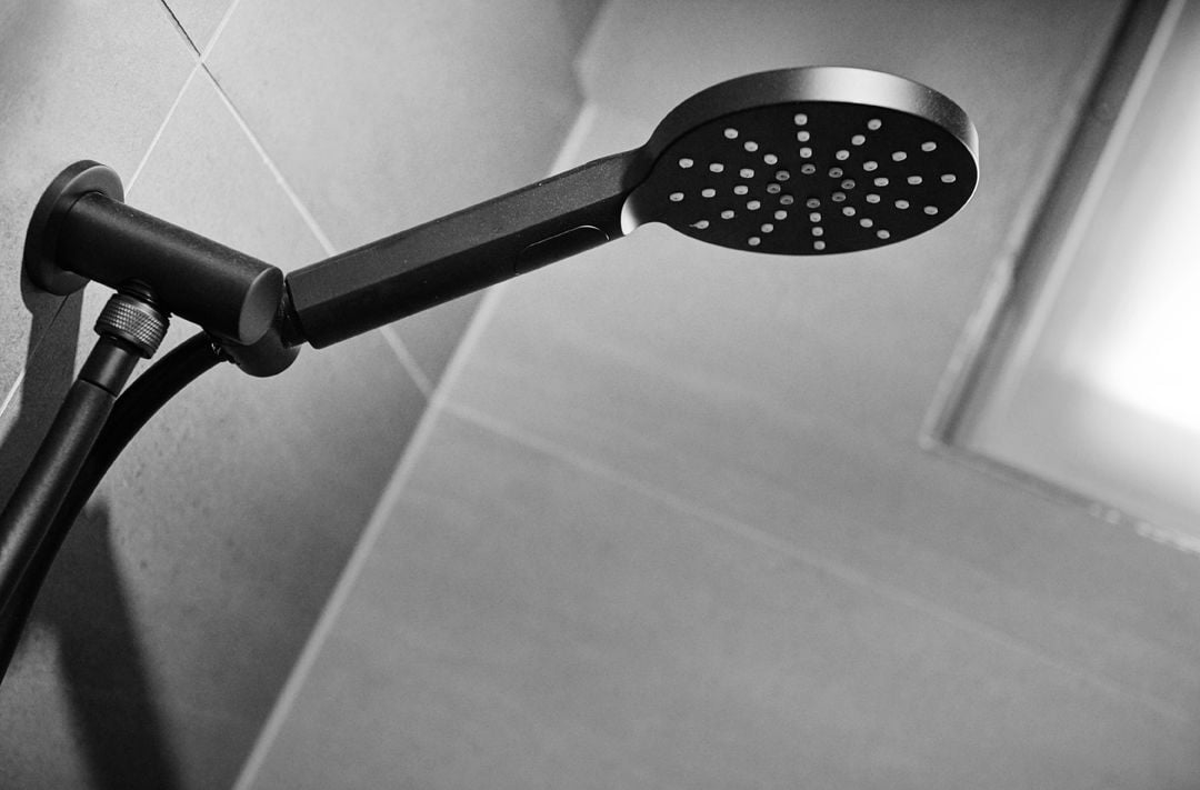 A modern showerhead with a sleek design, mounted on a wall with a tiled surface.