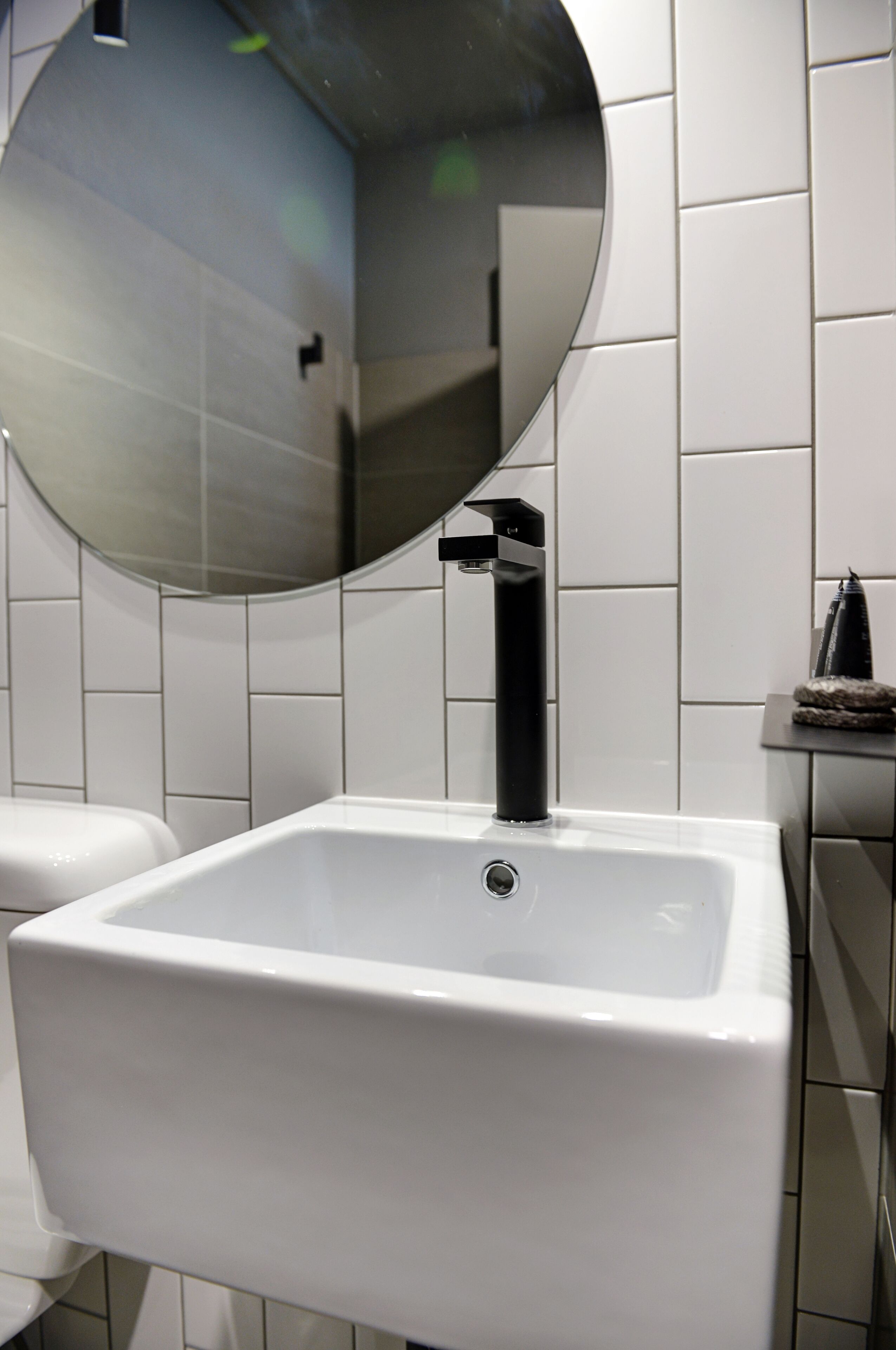 Een badkamer met een wit wastafel, een zwarte kraan en een ronde spiegel.