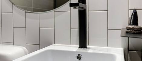 Een badkamer met een wit wastafel, een zwarte kraan en een ronde spiegel.