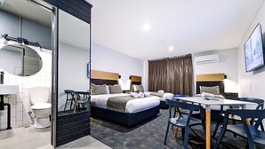 A modern hotel room with a bed, a dining table, chairs, a bathroom, and a large mirror.