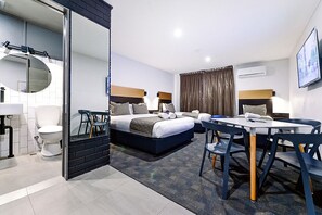 A modern hotel room with a bed, a dining table, chairs, a bathroom, and a large mirror.