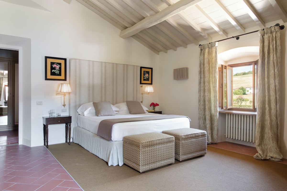 Een slaapkamer met een bed, nachtkastjes, een raam met gordijnen en uitzicht op de omgeving.