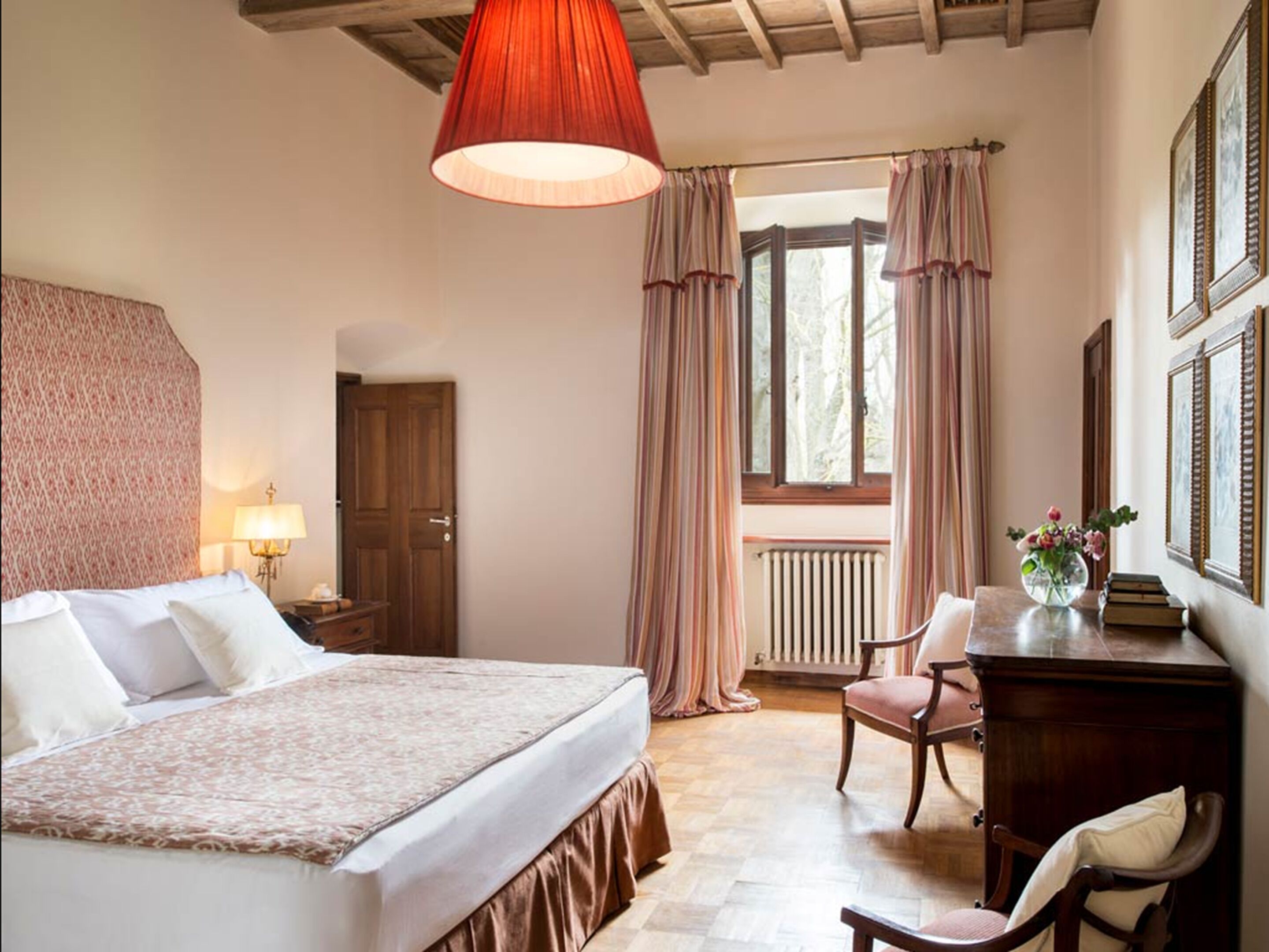 A bedroom with a bed, a desk, a chair, a window with curtains, and a radiator.