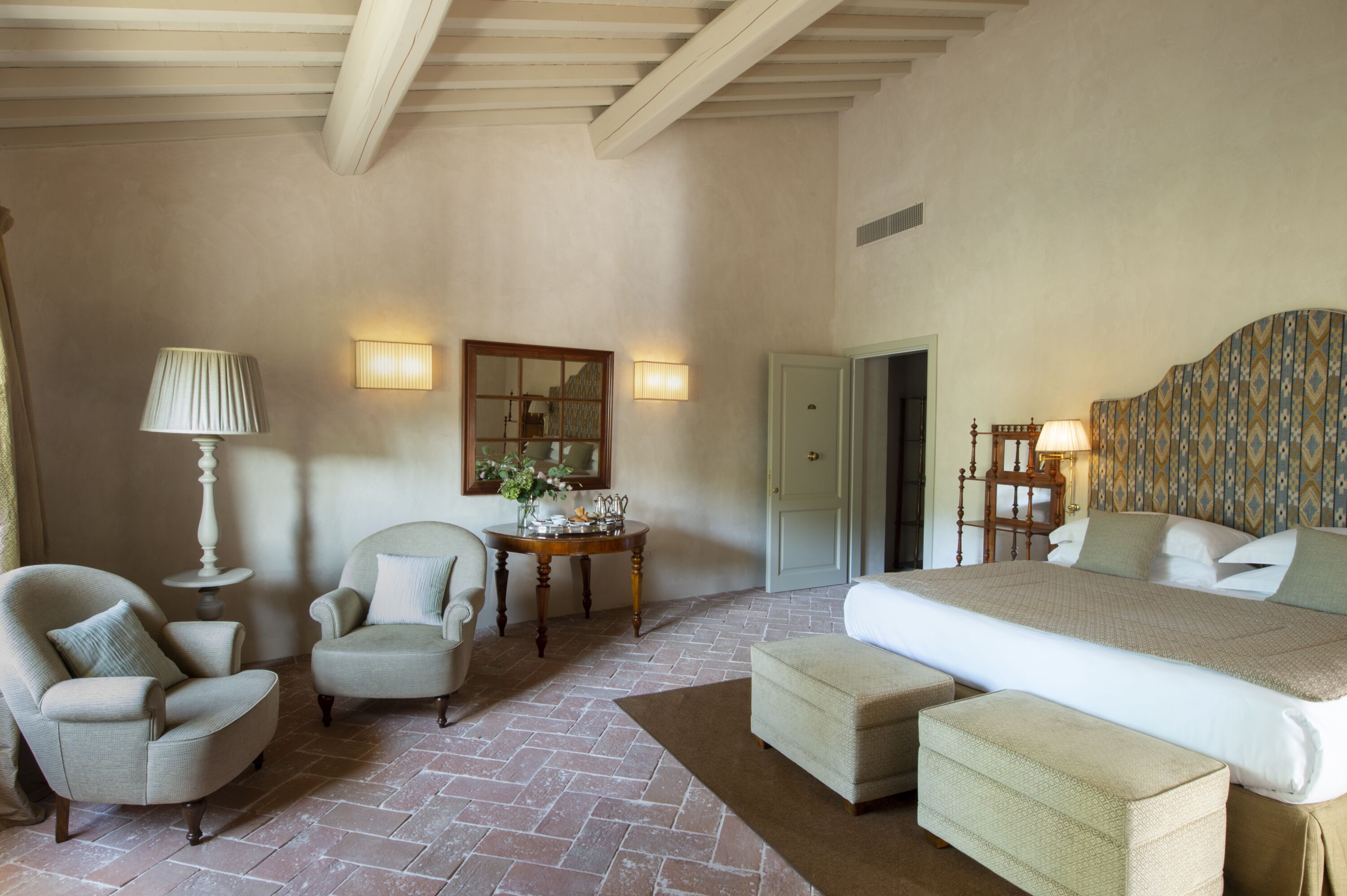 Habitación de hotel con una cama grande, dos sillones, una mesita con una lámpara y un espejo en la pared.