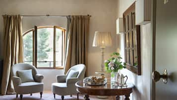 A room with two armchairs, a table with a tray of pastries, a lamp, and a mirror.