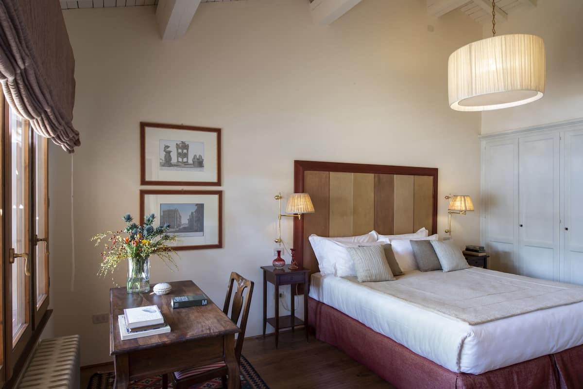 Een slaapkamer met een groot bed, bedlampen, een houten hoofdeinde, een bureau met stoel en ingelijste foto's aan de muur.