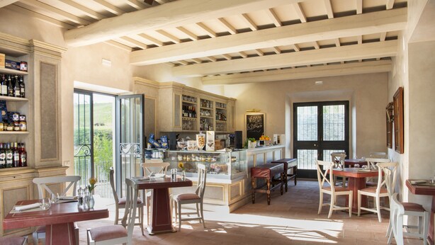 Un vaste espace dédié à la salle à manger, avec de nombreuses tables et chaises, un bar doté d’étagères remplies de bouteilles, et une grande fenêtre offrant une vue sur l’extérieur.