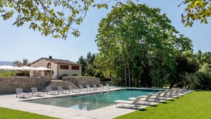 Une piscine avec des chaises longues, un mur en pierre et un bâtiment doté d’un toit en tuiles.