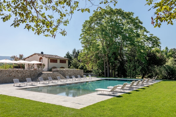 A swimming pool with lounge chairs, a stone wall, and a building with a tiled roof.