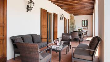 Un patio techado con muebles de mimbre, un muro de piedra y una zona de comedor con sillas y una mesa.