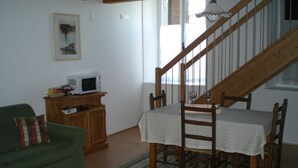 A living room with a green sofa, wooden dining table with chairs, a wooden cabinet, and a staircase. - Agriturismo Colutta (Manzano)