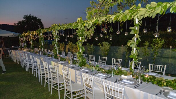 A long outdoor dining area with white tables and chairs, decorated with hanging glass ornaments and greenery. - Agriturismo Colutta (Manzano)