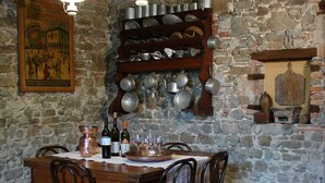 A rustic dining area with a stone wall, wooden table, and chairs. There are hanging lights, a wine rack, and a framed picture on the wall. - Agriturismo Colutta (Manzano)