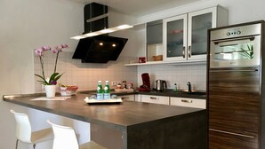 Et moderne køkken med en central ø, hvide barstole, rustfrie stål-apparater og et backsplash i hvide fliser.