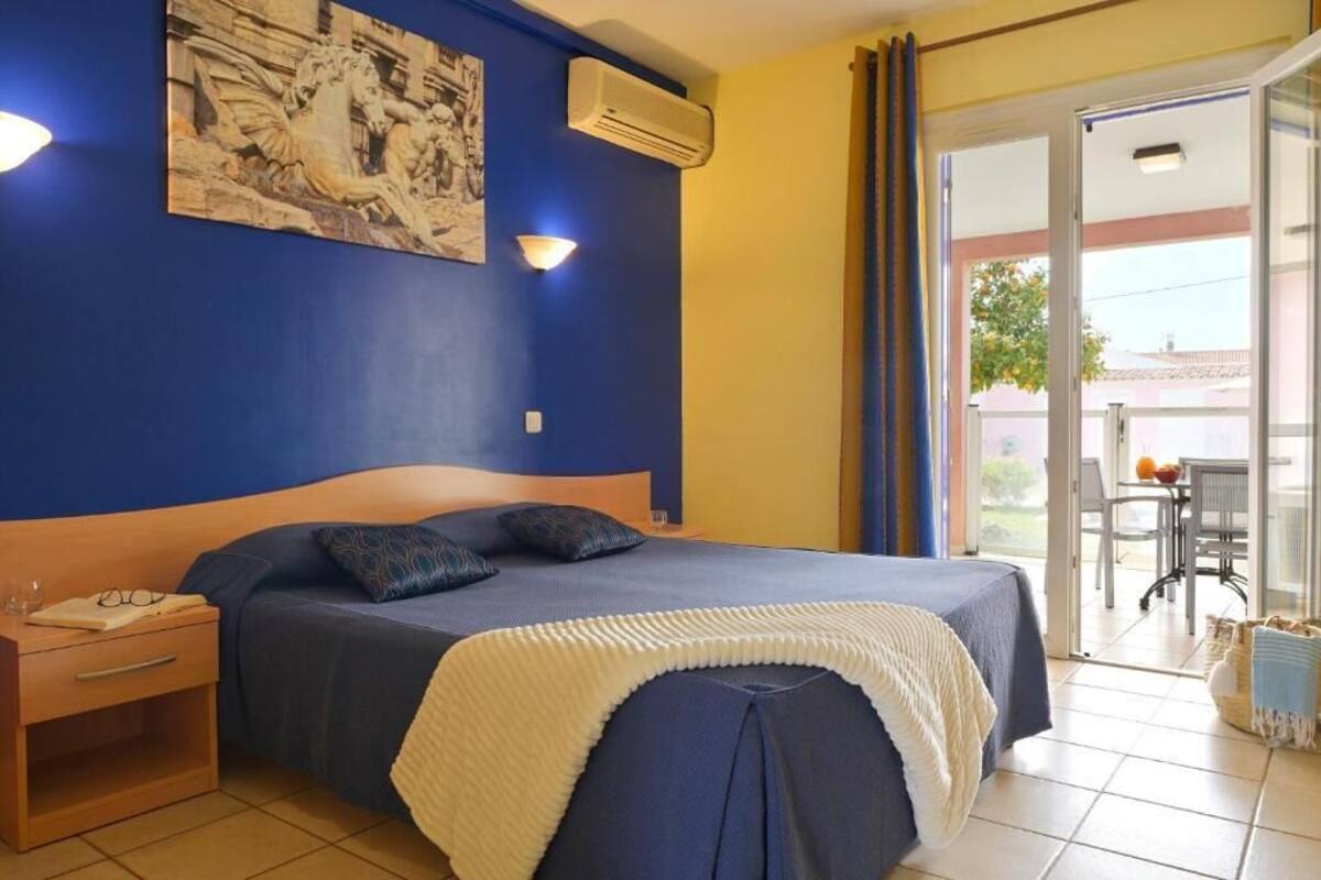 Une chambre à coucher comprenant un lit, une table de chevet, un climatiseur fixé au mur et une grande fenêtre avec des rideaux.