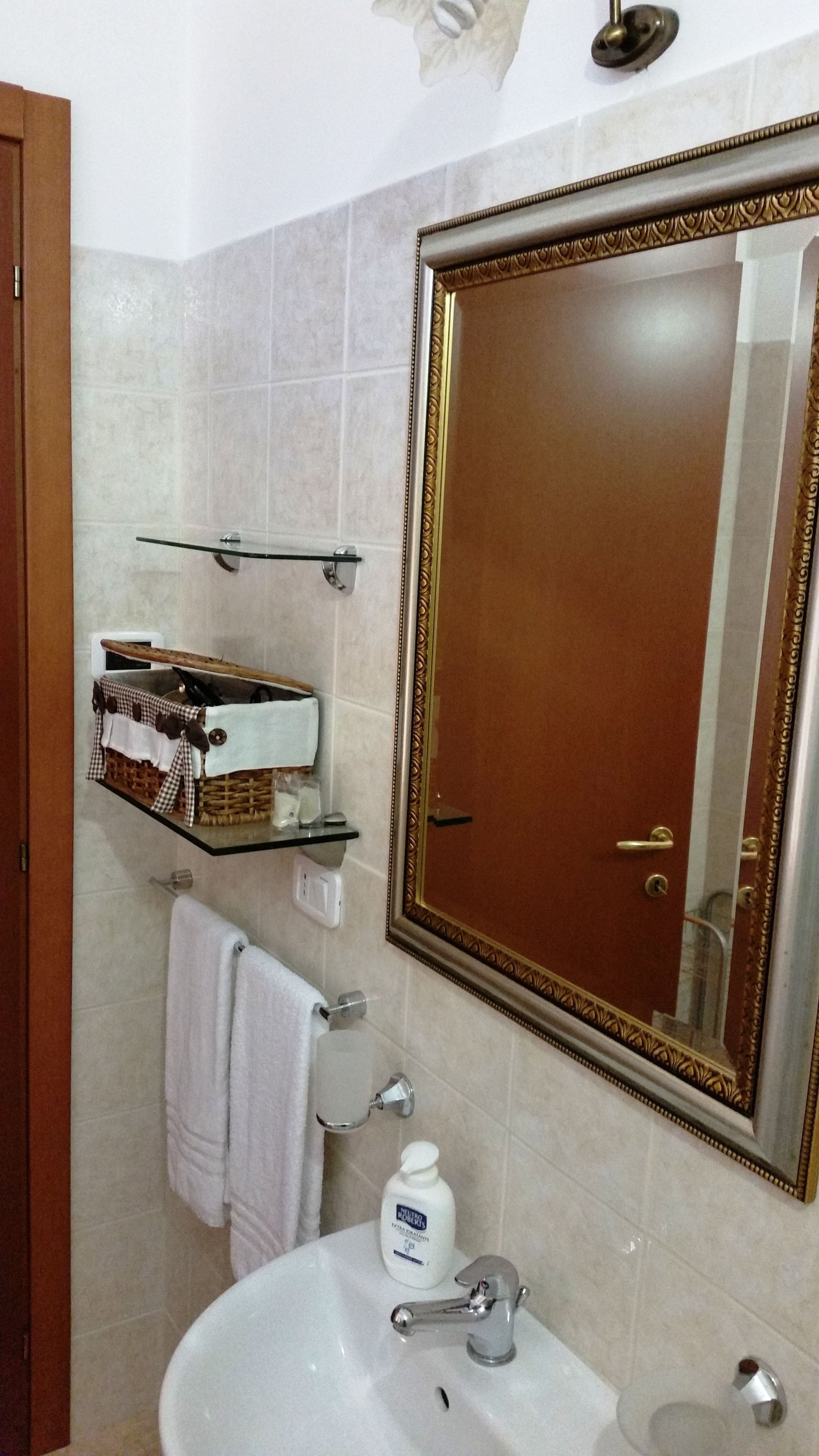 Ein Badezimmer mit einem großen Spiegel, einem Waschbecken, einem Handtuchhalter und einem Ablagebereich für Toilettenartikel.