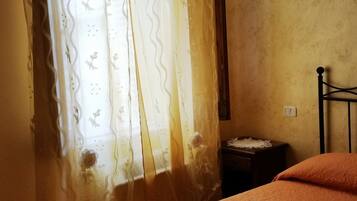A room with a bed, a nightstand, a wall-mounted light, and a window with curtains.