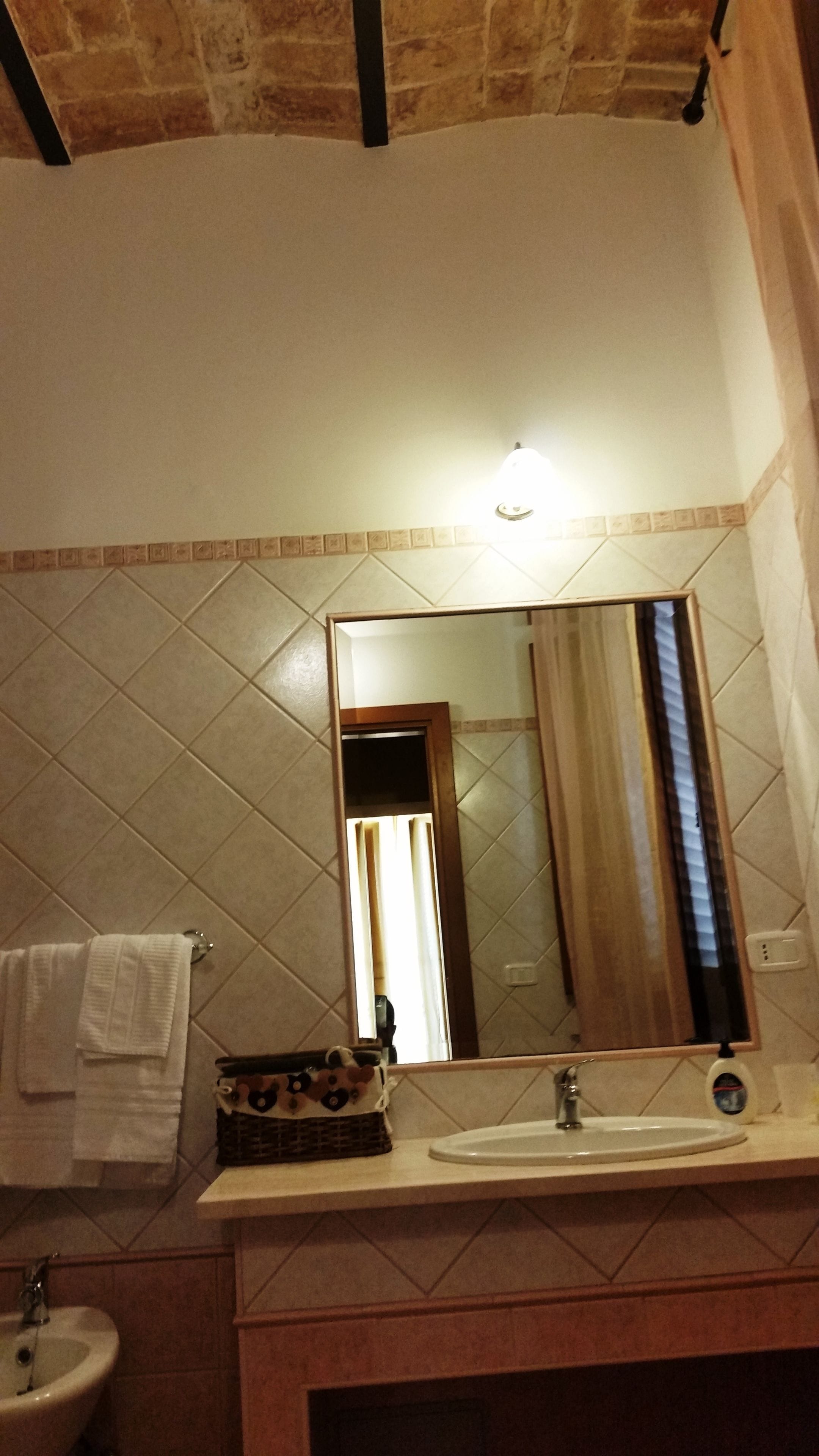 Une salle de bain avec un mur carrelé, un lavabo, un miroir et une serviette accrochée au mur.
