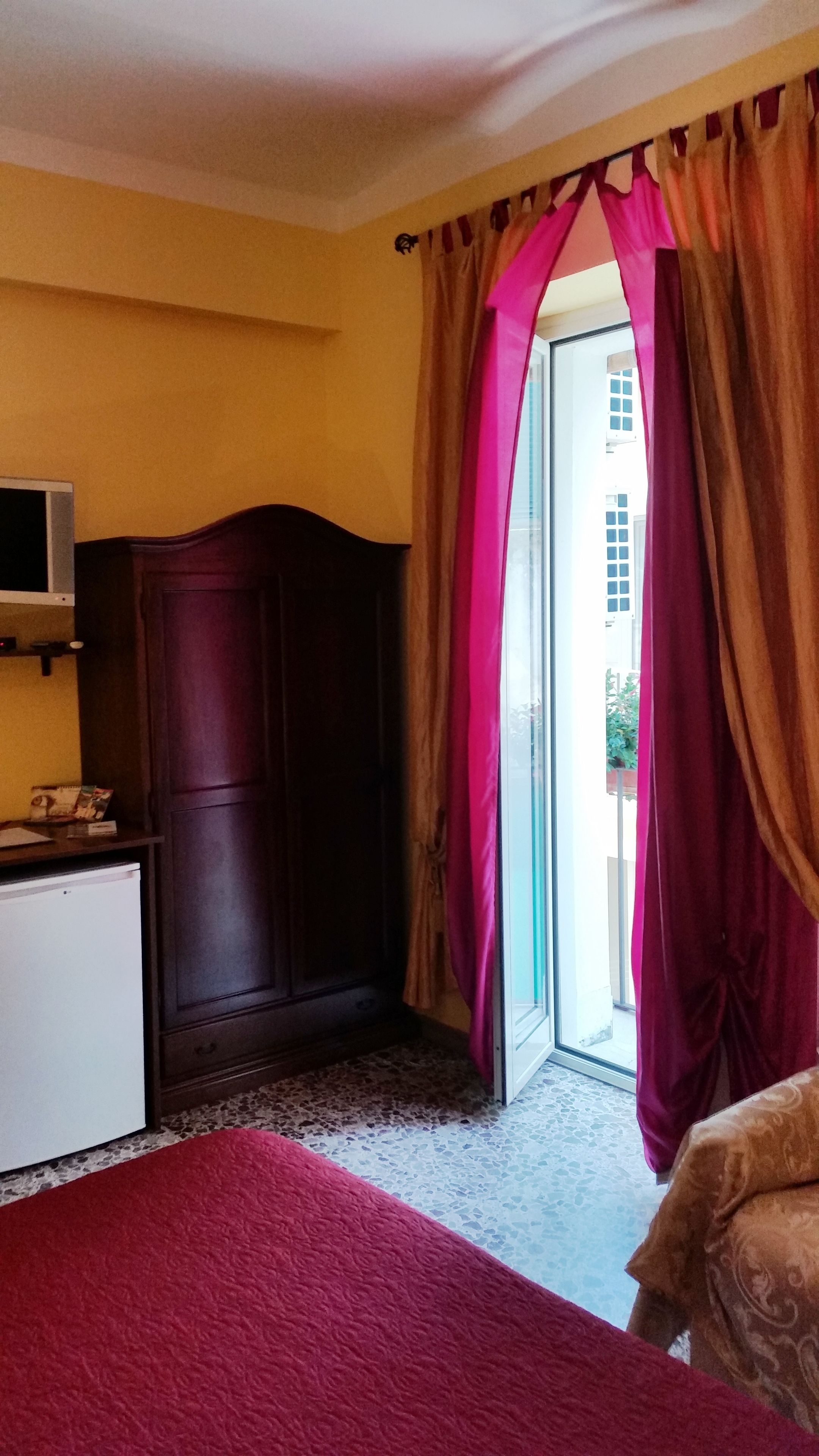 A hotel room with a bed, a wardrobe, a small table with a phone, and a view of the outside through a glass door.