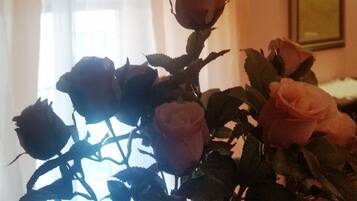 A vase with roses in a room with a window and curtains.
