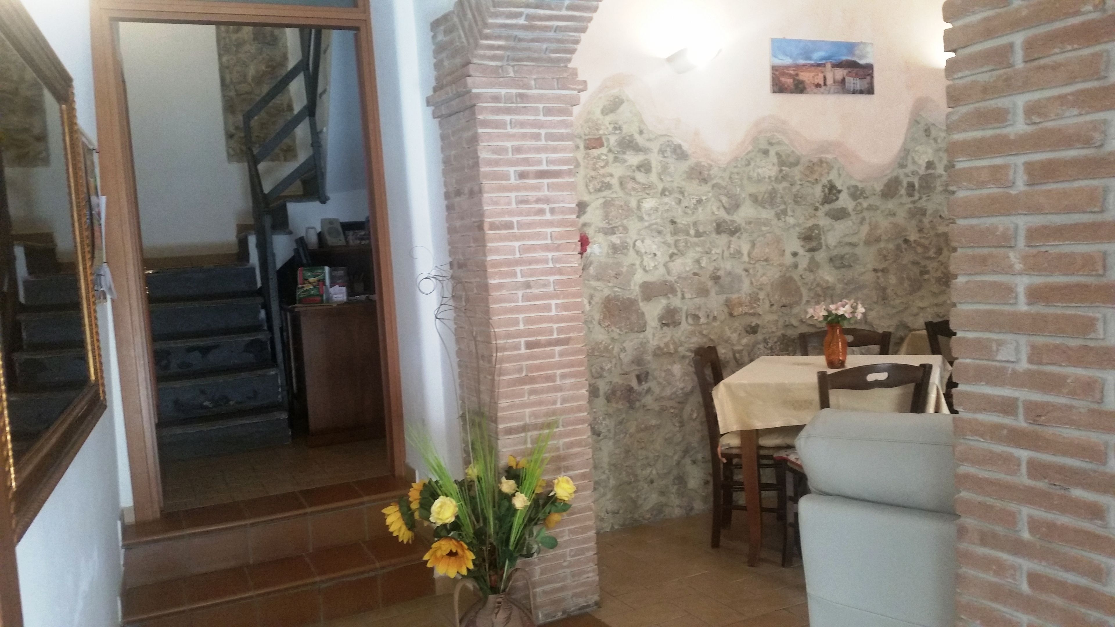 Un comedor con pared de ladrillo, una mesa con sillas y un florero con flores.