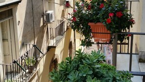 Uma rua estreita no centro urbano, com edifícios que apresentam sacadas, aparelhos de ar condicionado e plantas em vasos.