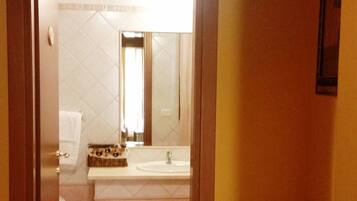 A narrow hallway leading to a bathroom with a toilet, sink, and mirror.