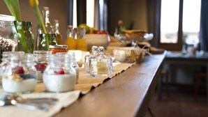 A wooden table with glass jars containing food items, a bowl of fruit, and a candle holder. - Agriturismo Borgoluce (Susegana)