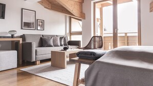 A modern living room with a grey sofa, wooden coffee table, and a wicker chair. There is a large window with a view of the outside. - Alpin Life Hotel Gebhard (Fiss)