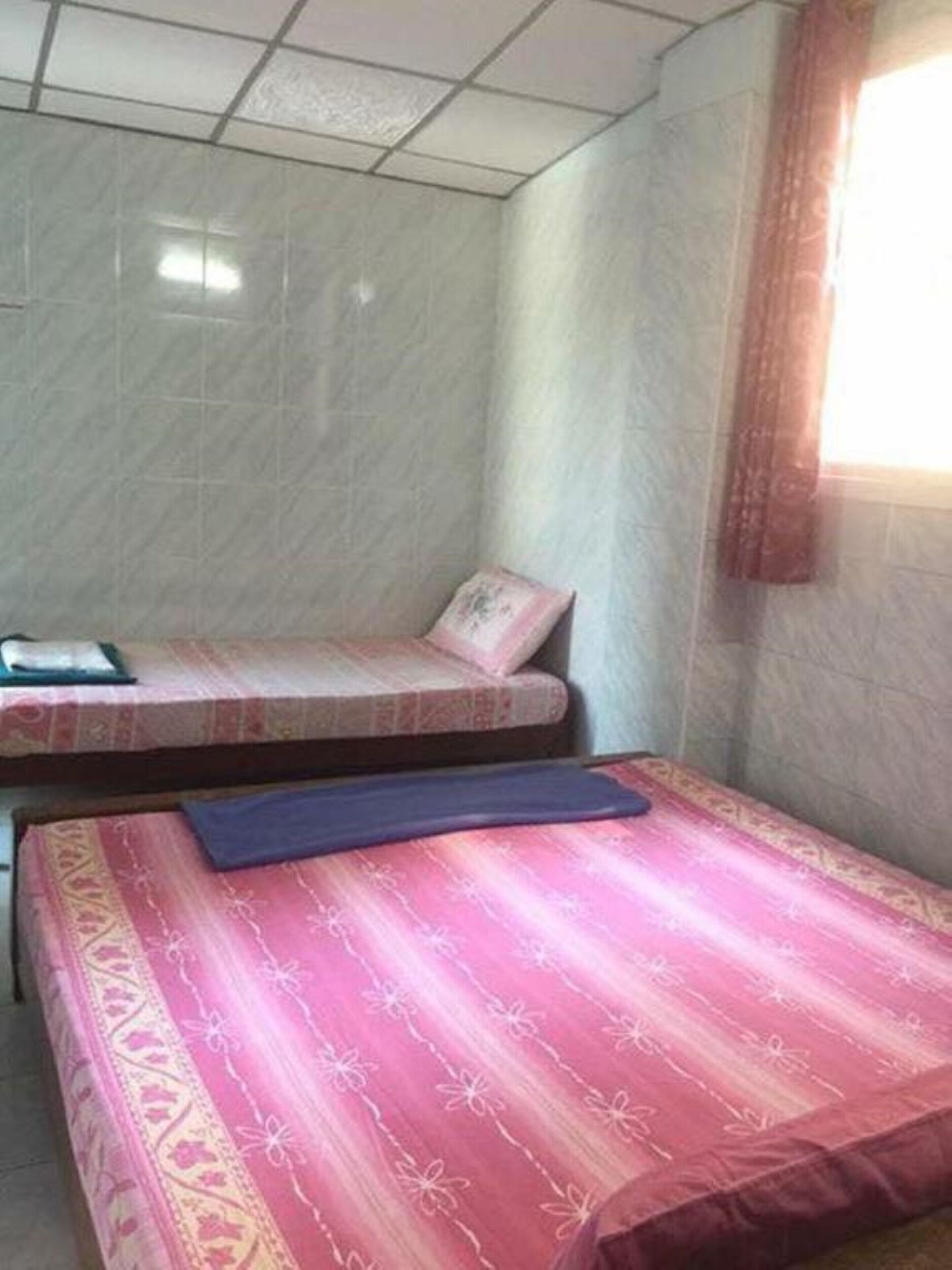 Una habitación con dos camas, una con colcha estampada y la otra con sábanas lisas.