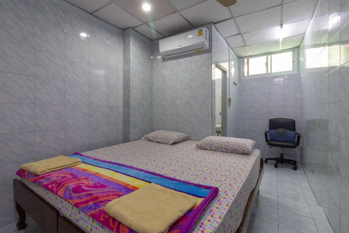 A hotel room with a bed, a chair, and an air conditioning unit.
