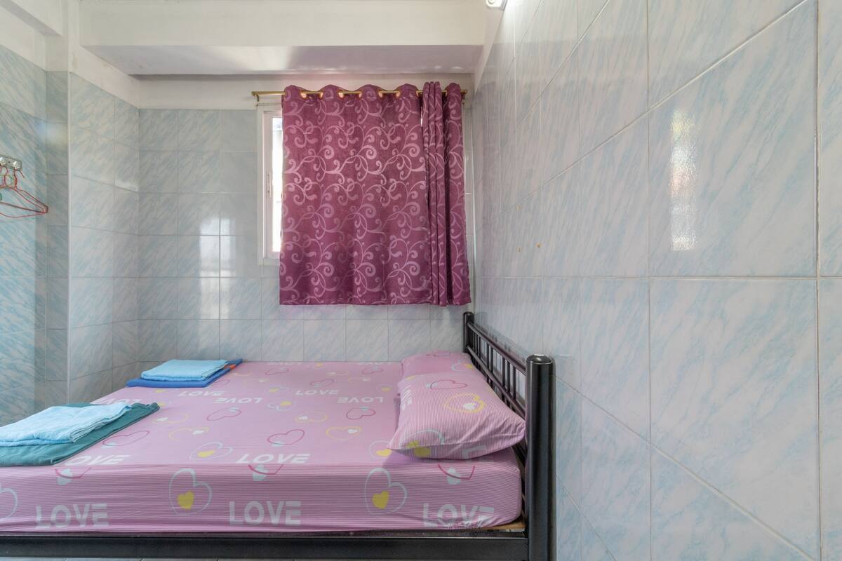 A small, neatly arranged bedroom with a bed, pillows, and a window with curtains.