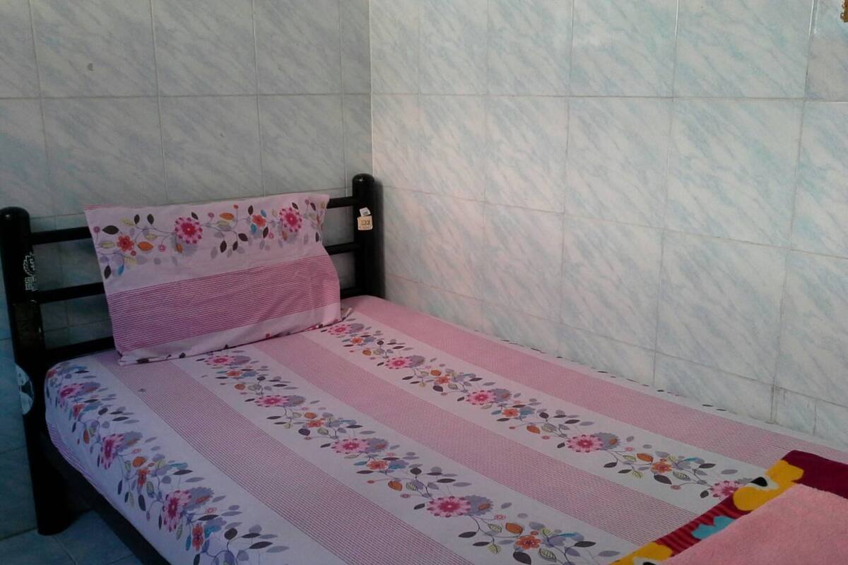 A small bed with a floral bedspread and a matching pillow, set against a tiled wall.