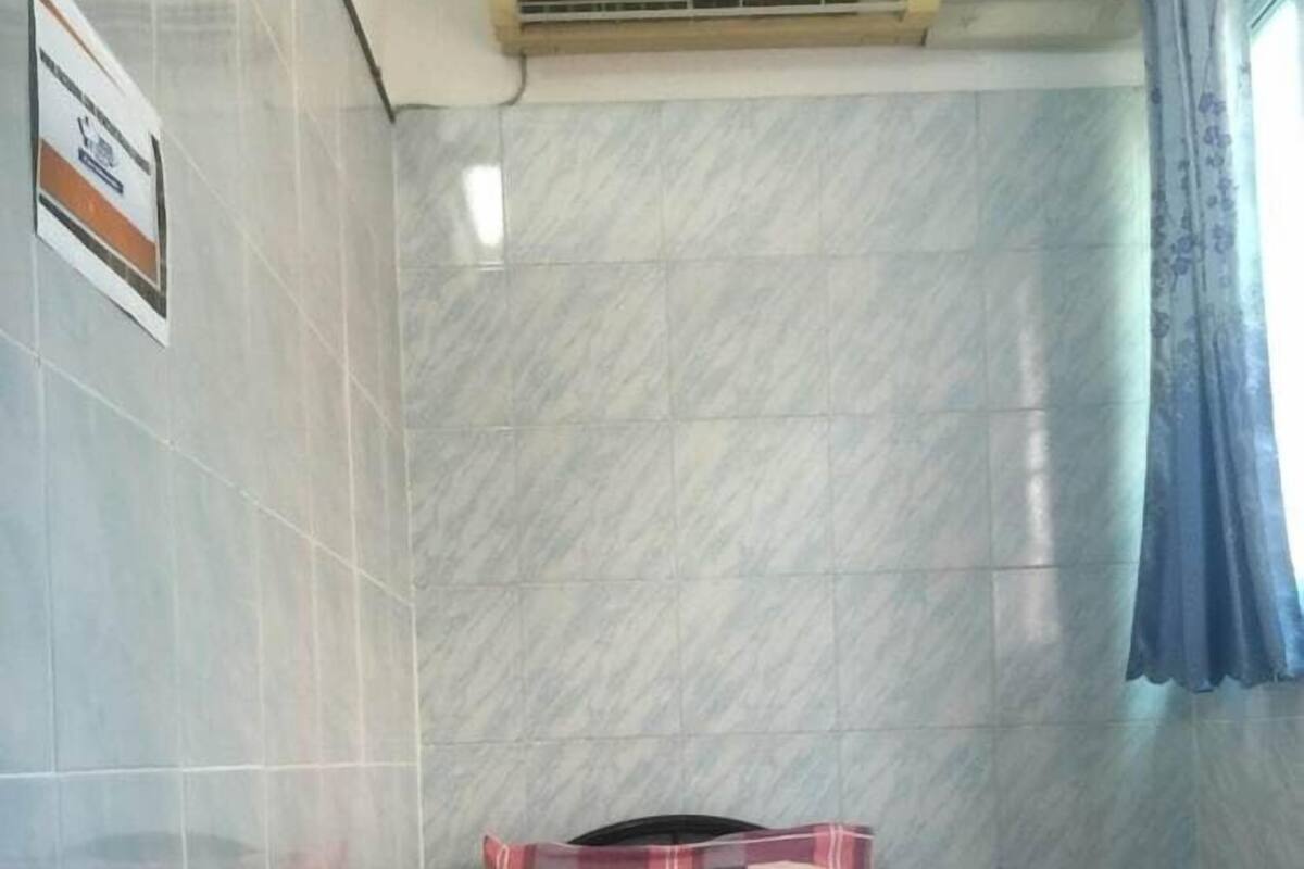 A small, tiled room with a bed, a pillow, a blanket, and an air conditioning unit.