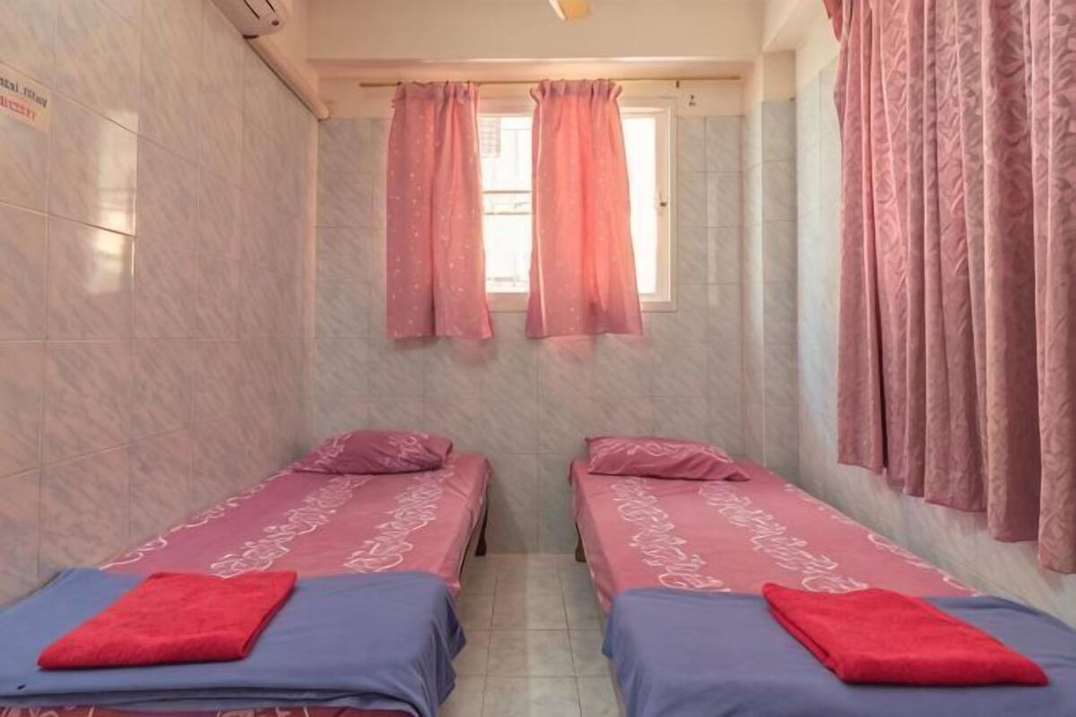 A small, single-room hotel with two beds, each with a red towel and a patterned bedspread.