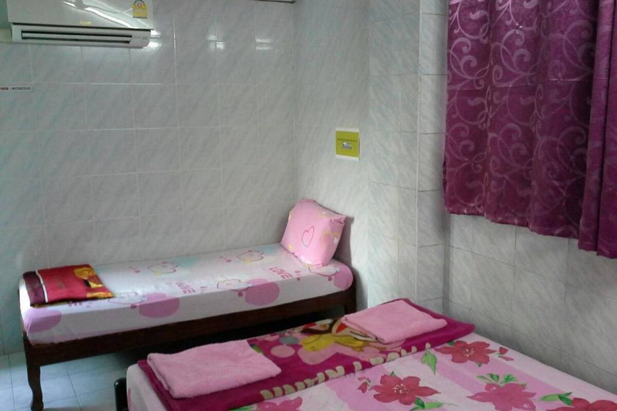 A small, clean room with a bed, a bedside table, and a window with purple curtains.