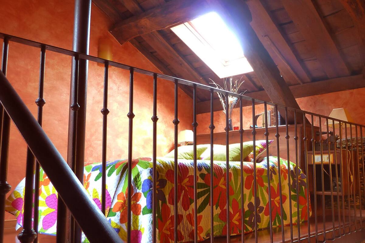 A room with a bed, a stone wall, a wooden ceiling, and a skylight.
