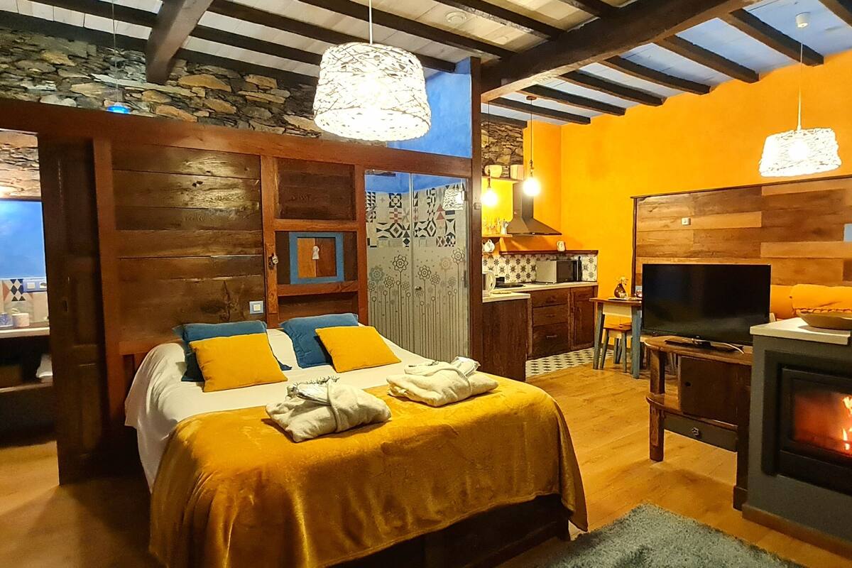 A cozy bedroom with a bed, a fireplace, and a stone wall.