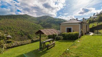 A rustic house with a thatched-roof structure and a stone bench in a lush green valley.