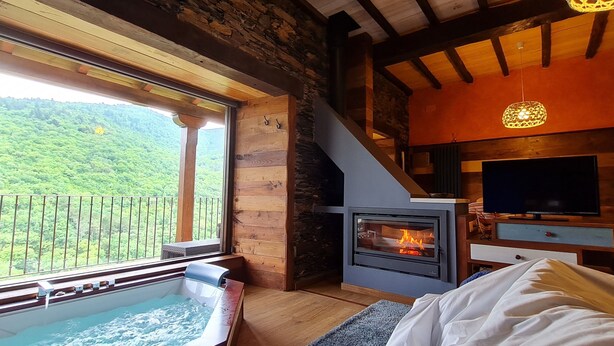 A cozy room with a stone fireplace, a large window with a balcony, and a hot tub. - El Bosque de las Viñas (Boal)