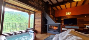 Ein gemütliches Zimmer mit Kamin aus Stein, einem großen Fenster mit Balkon und einer Whirlwanne.