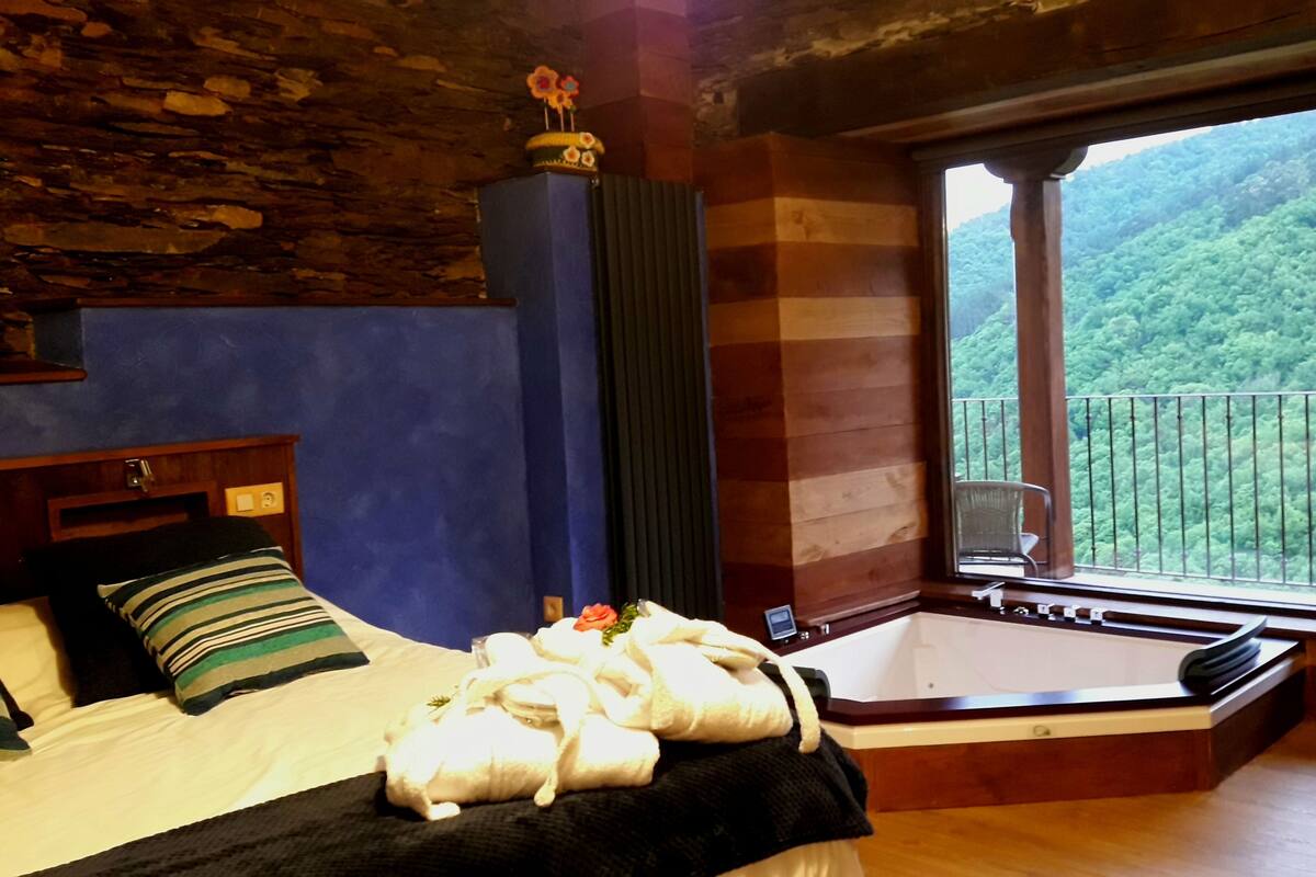 A bedroom with a large bed, a wooden headboard, a window with a view of a forest, and a wooden floor.